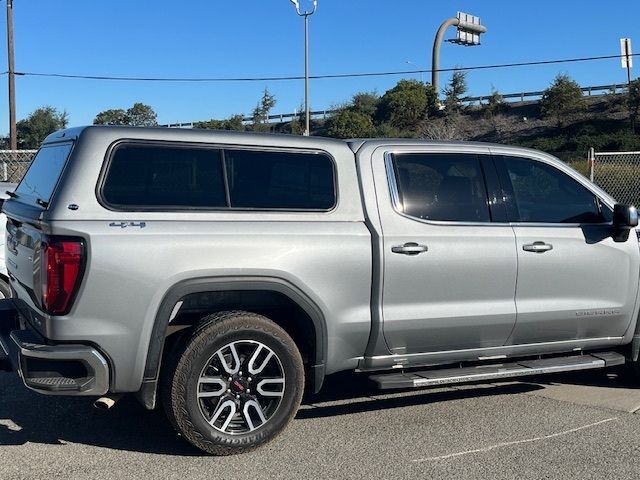 A silver GMC crew cab pickup truck with a matching camper shell parked in an outdoor lot on a sunny day.
