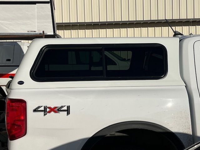 Side view of a white truck bed camper shell with a tinted sliding window and a 4x4 emblem on the truck body.