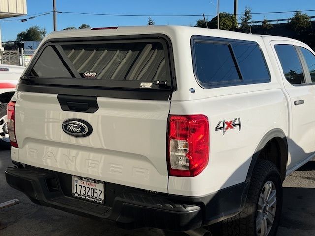 A white Ford Ranger 4x4 pickup truck with a camper shell parked outdoors.