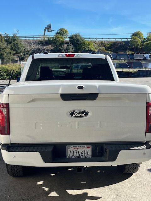 A white Ford pickup truck seen from behind, featuring a color-matched tonneau cover and California license plate.