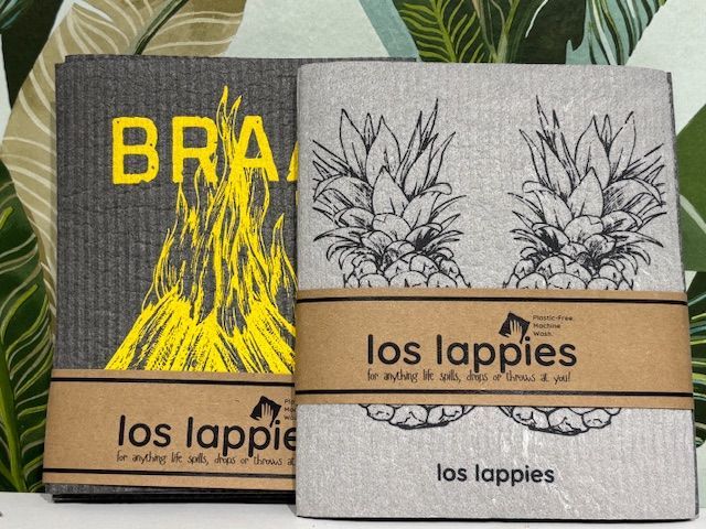 Two Los Lappies cleaning cloths: gray with yellow text and pineapples, brown paper bands.