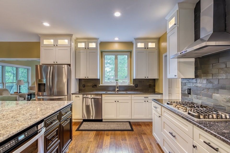 A kitchen with white cabinets , stainless steel appliances , granite counter tops and hardwood floors.