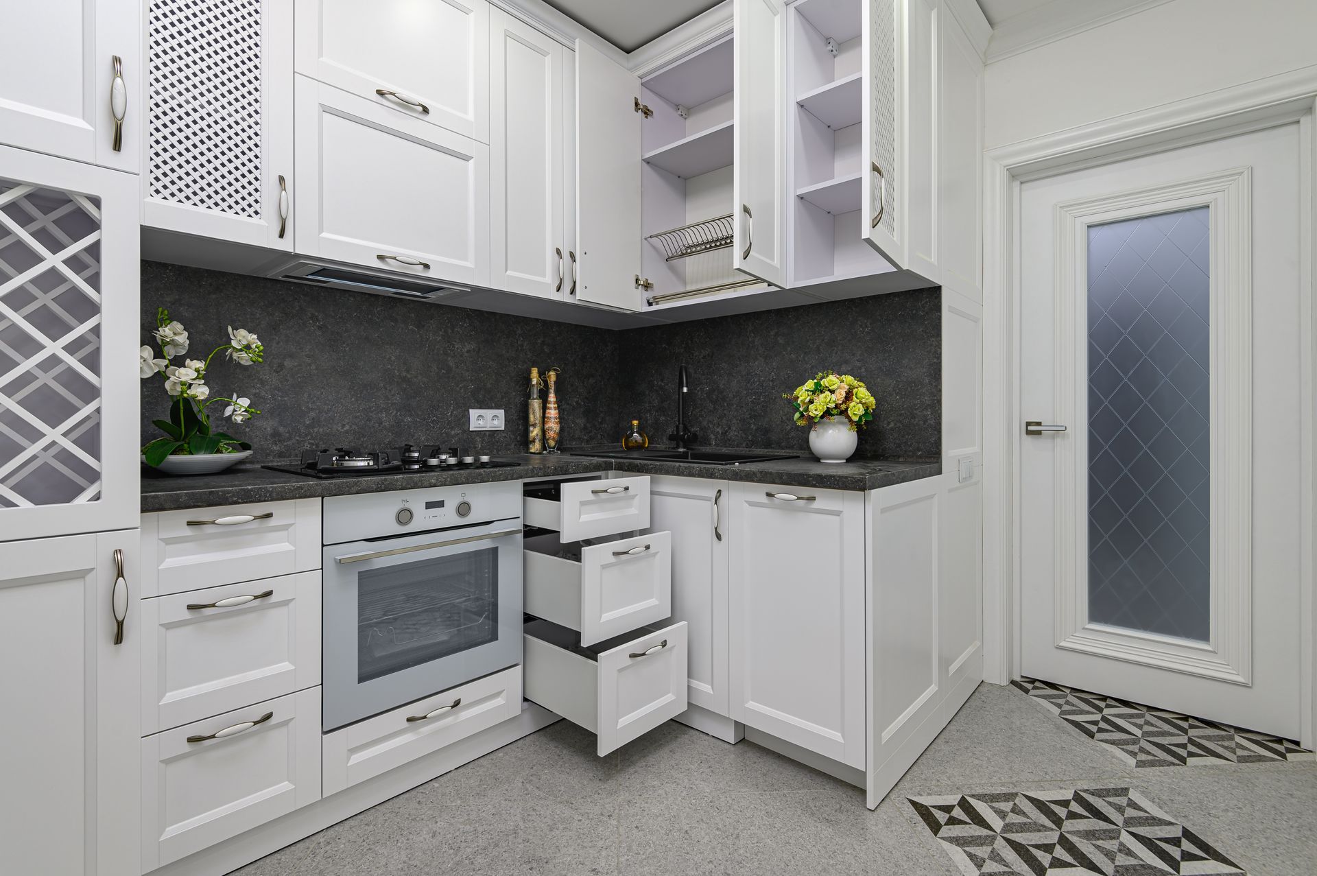 A kitchen with white cabinets , a stove , a sink and drawers.