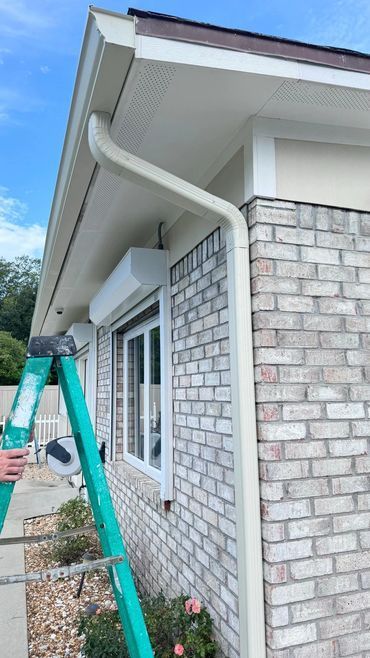 A person is standing on a green ladder next to a brick house.