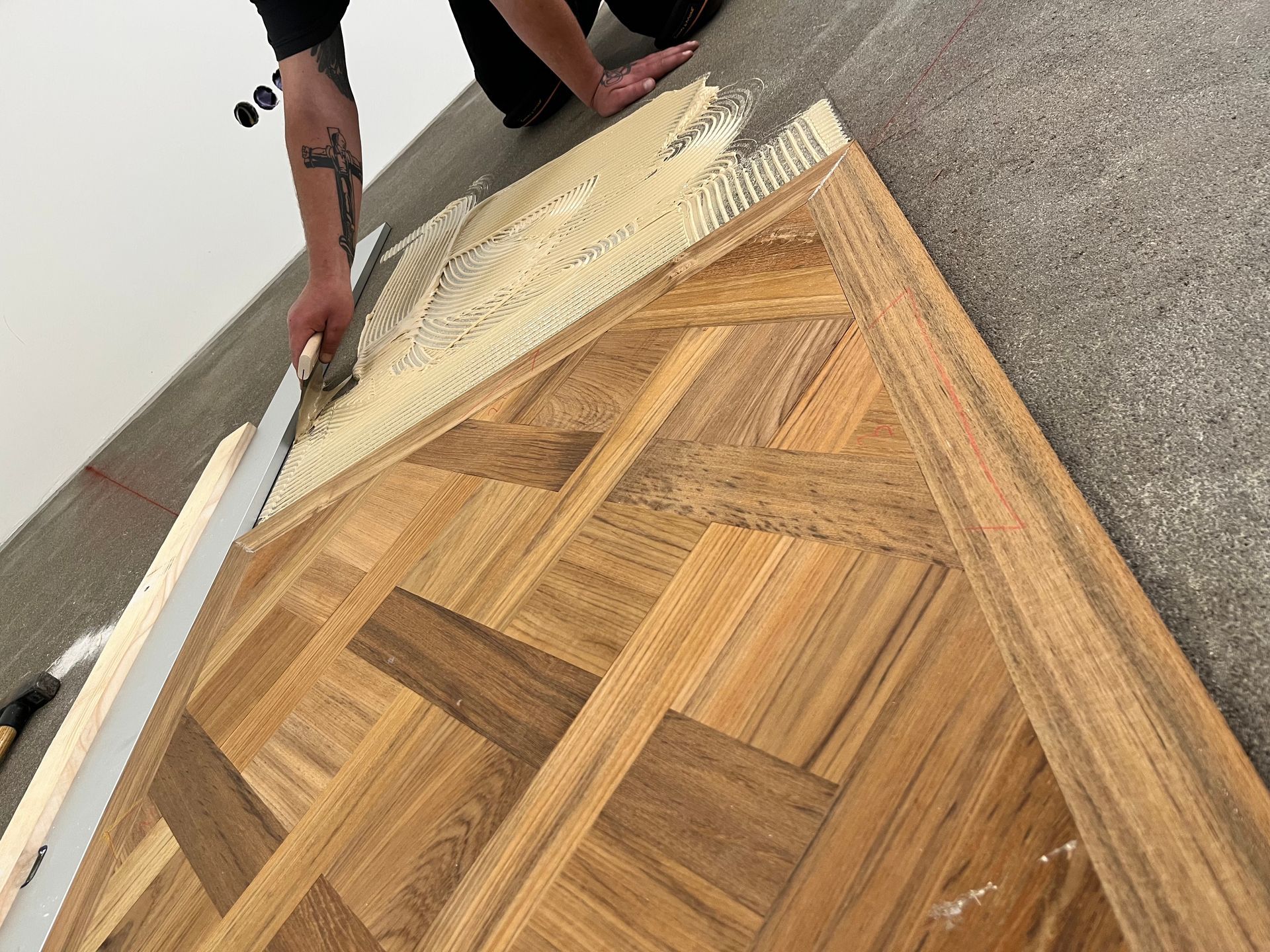 Person, die Fischgrätparkett verlegt, verteilt Klebstoff mit einer Kelle. Das Holz ist hellbraun.