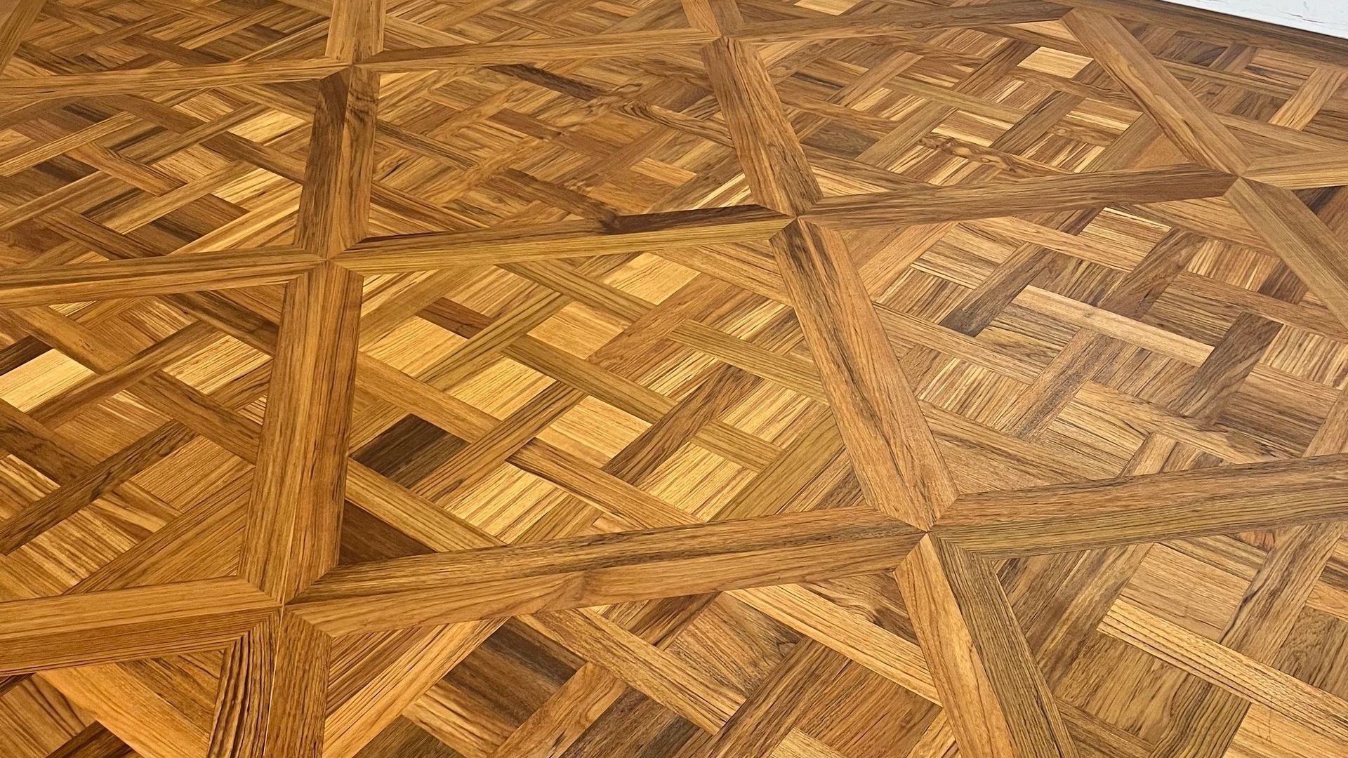 Nahaufnahme eines Holzbodens mit einem geometrischen Korbgeflechtmuster aus abwechselnd hell- und dunkelbraunem Holz.