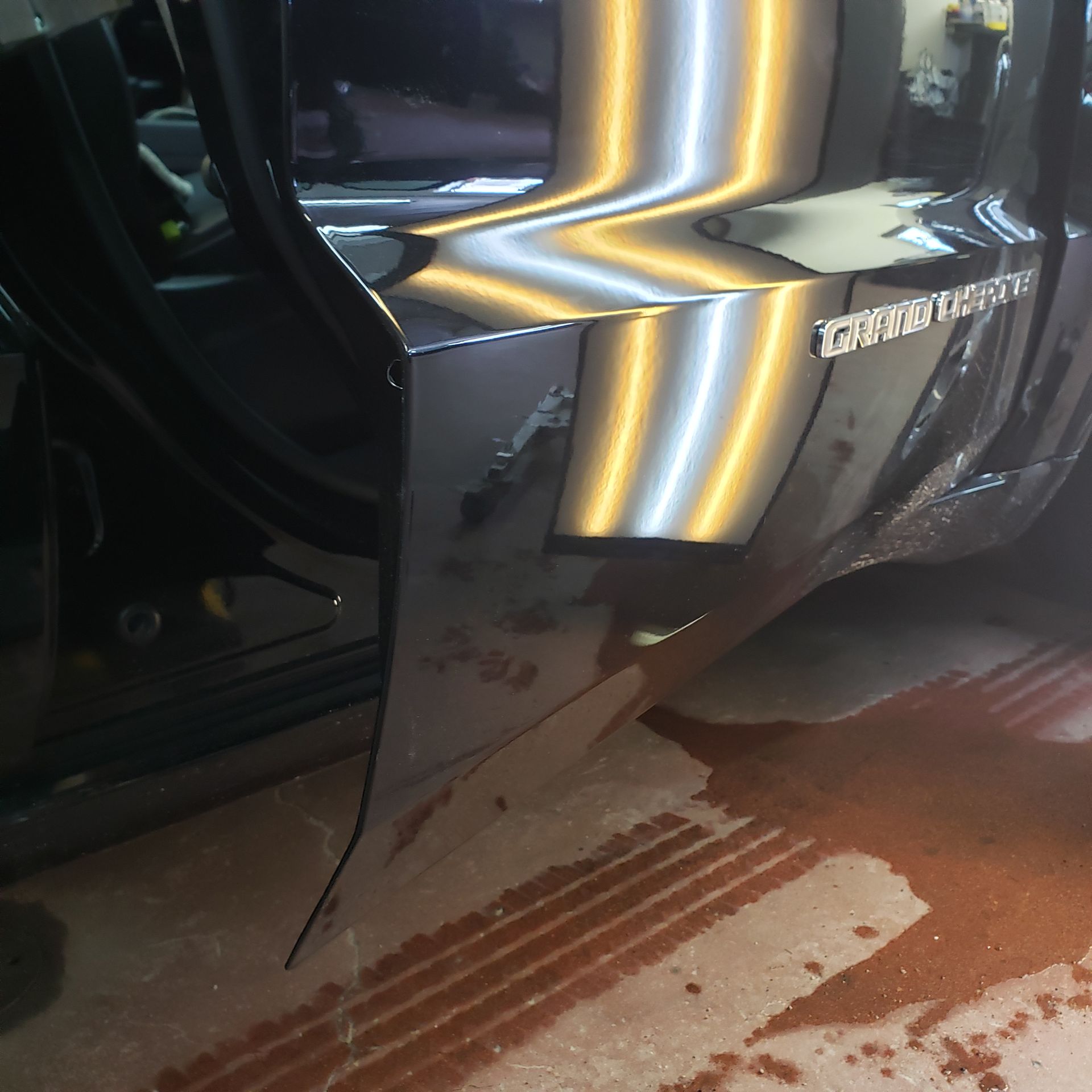 A black car with a damaged bumper is parked in a garage