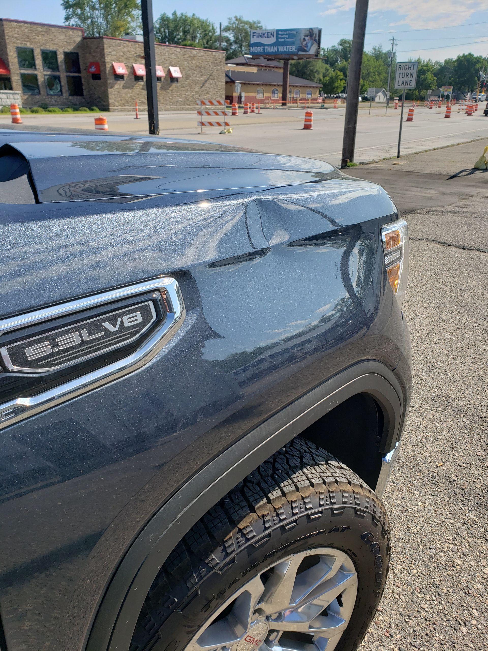A black truck with a damaged hood is parked in a parking lot.