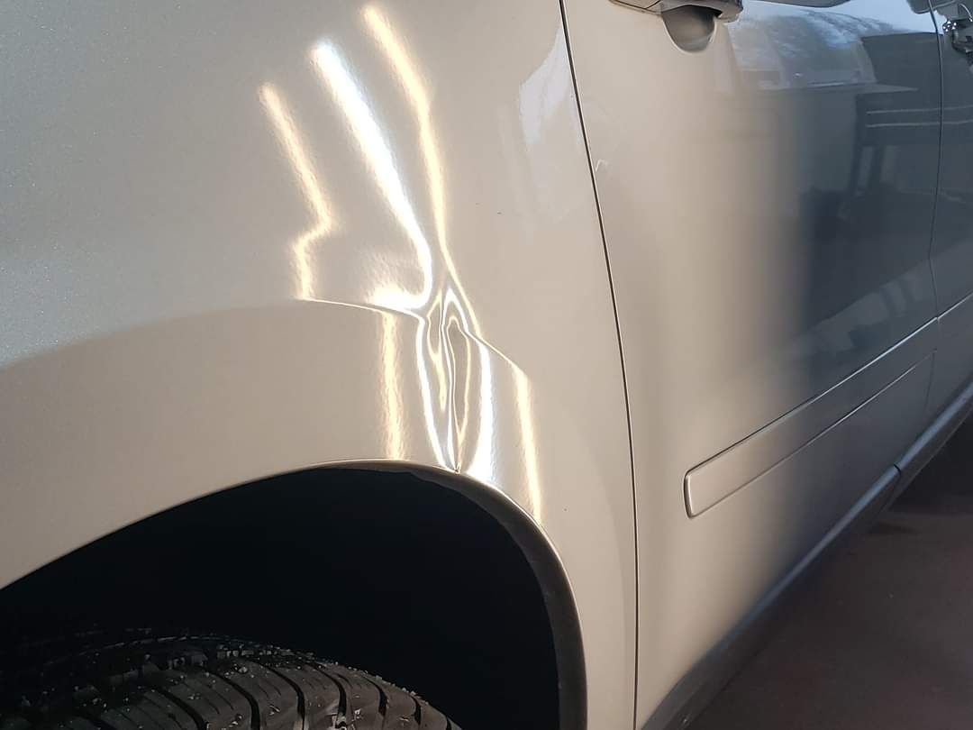 A silver car with a damaged fender is parked in a garage.