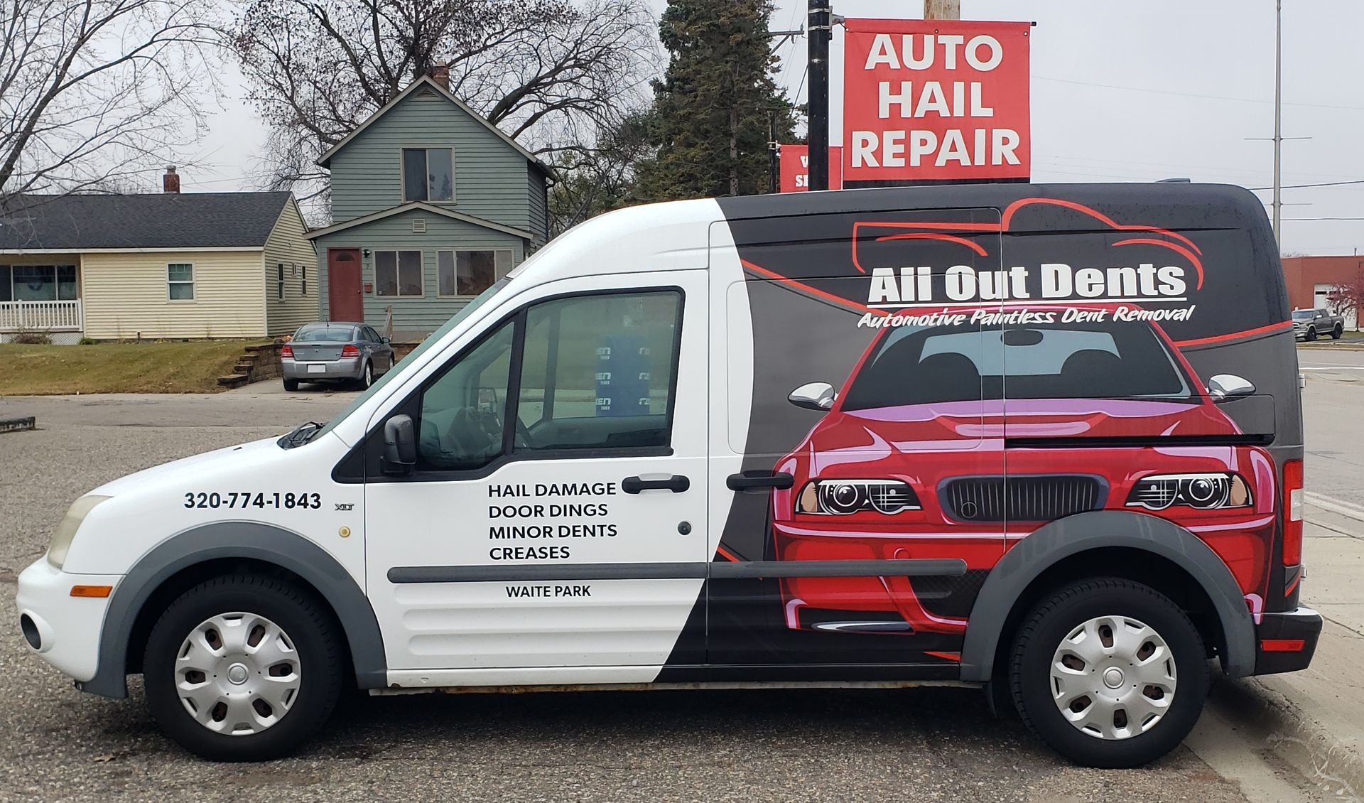 An auto hail repair van is parked in front of a building