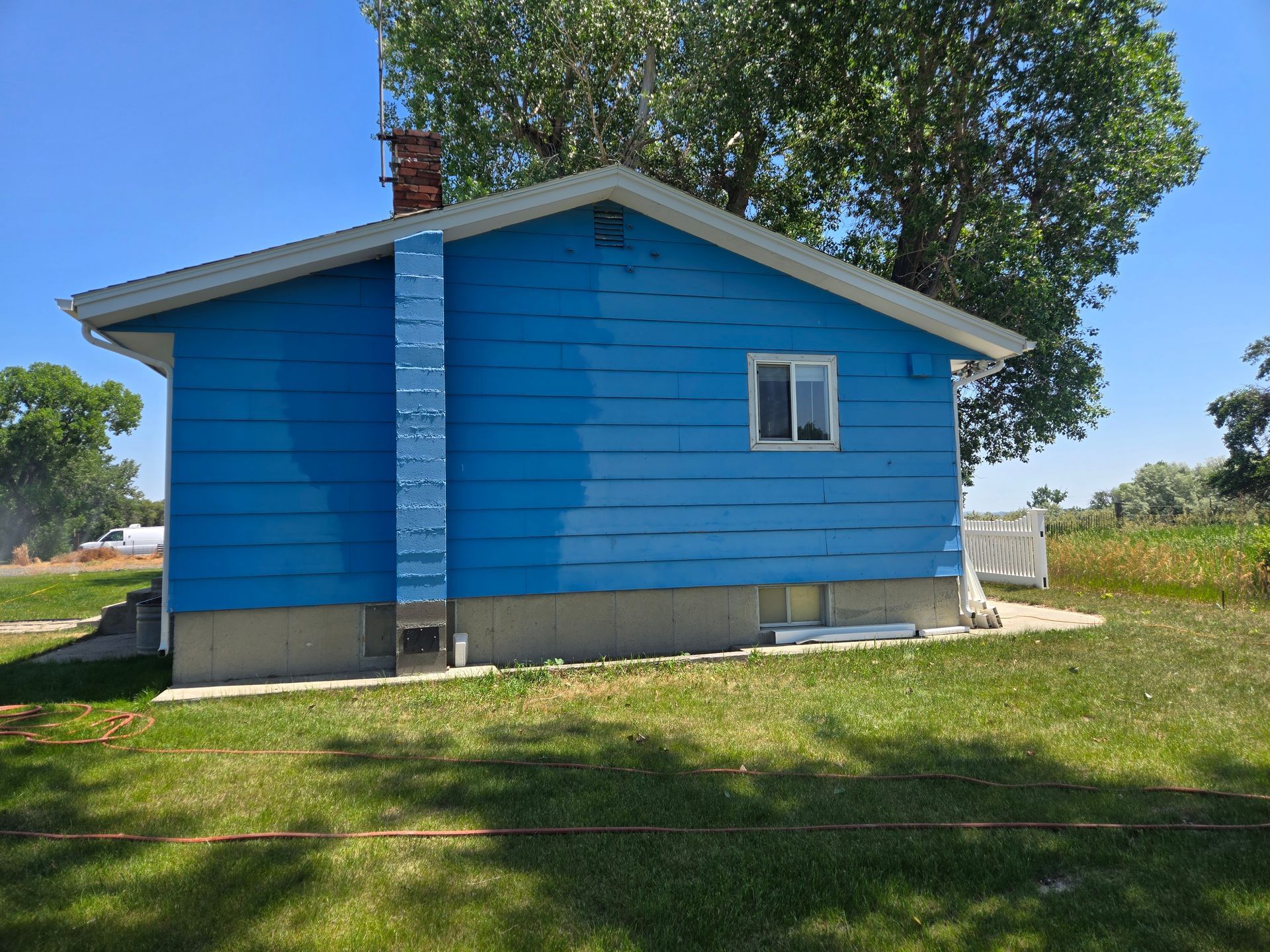 Blue house with white trim, chimney, and a small window against a blue sky. Green grass in the yard.