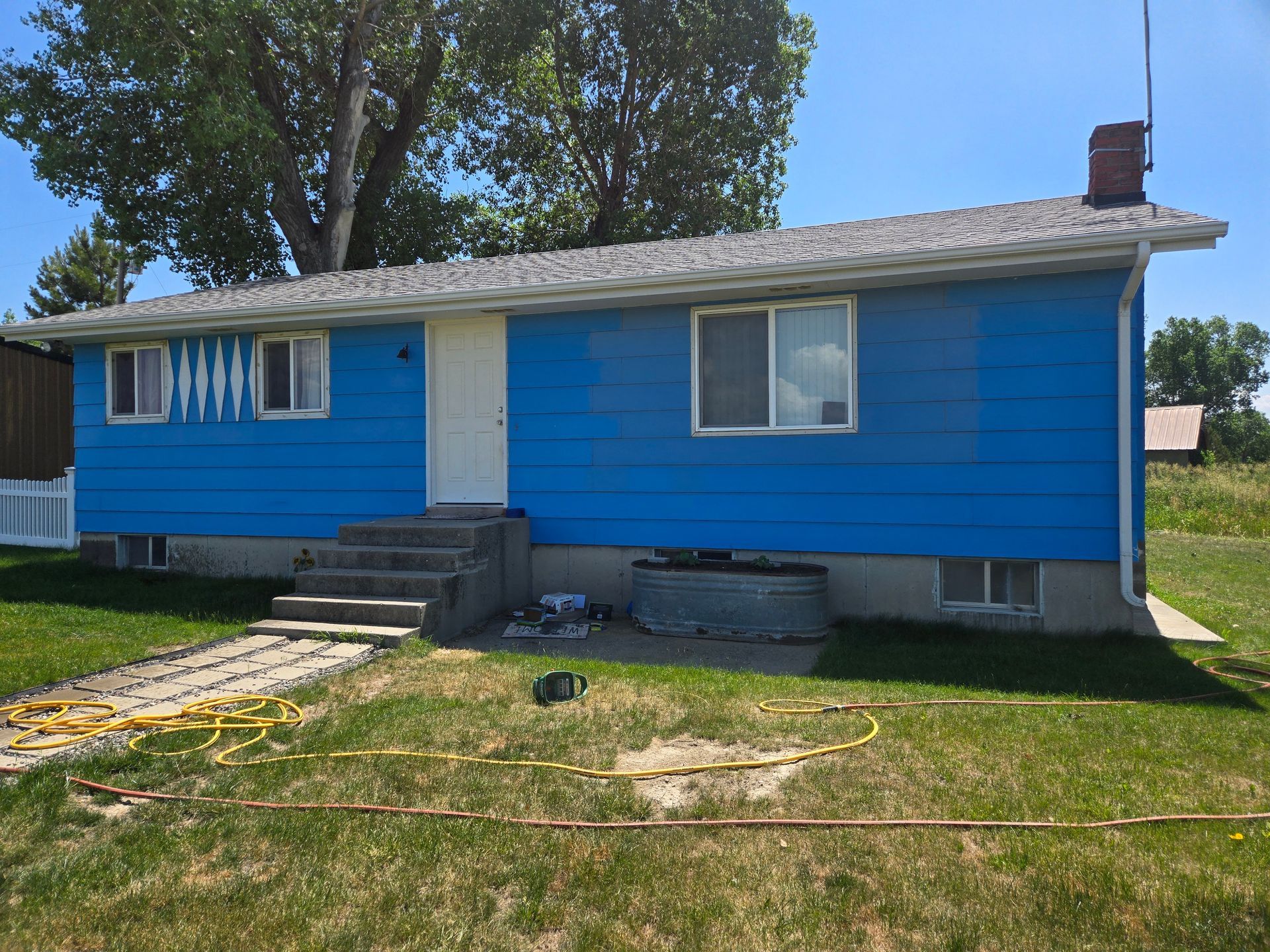 Blue house with white trim, concrete steps, and a chimney on a sunny day.