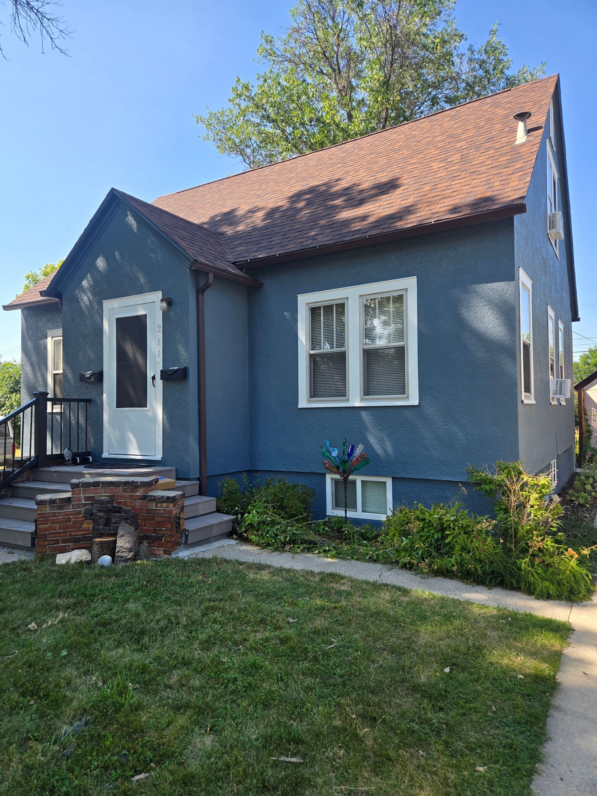 Blue stucco house with brown roof and white trim. Steps lead to a white front door. Green lawn.