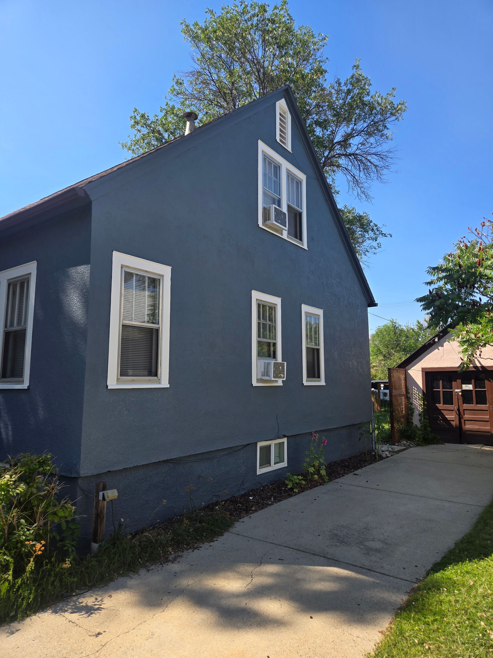 Blue house with white trim and windows, next to a concrete driveway.