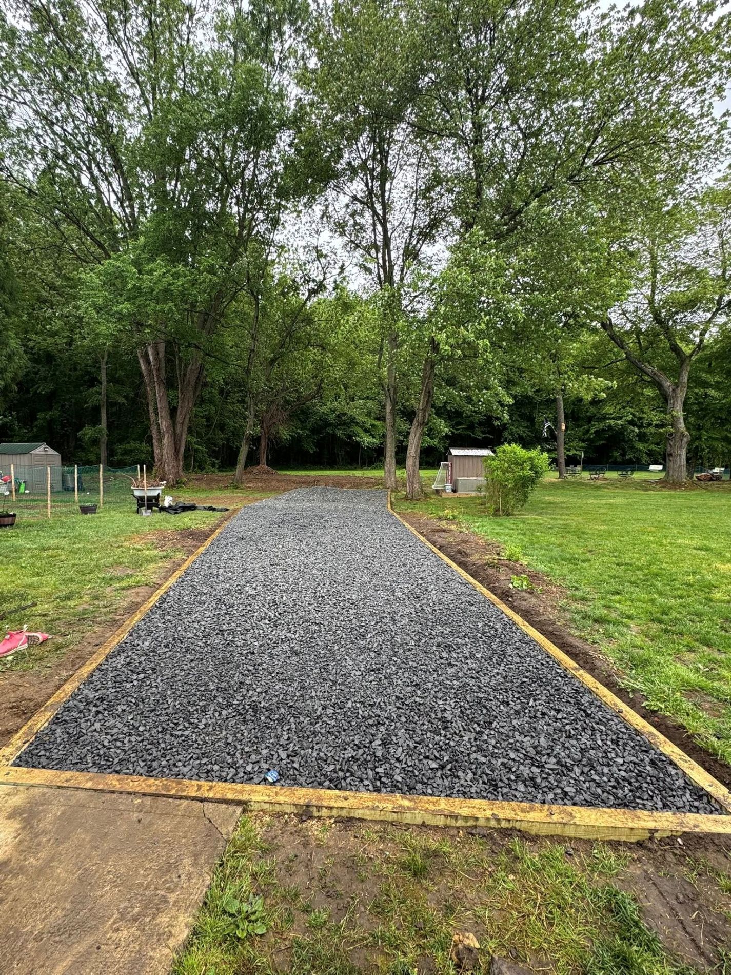 A gravel pathway bordered by wood in a grassy yard, trees in the background.