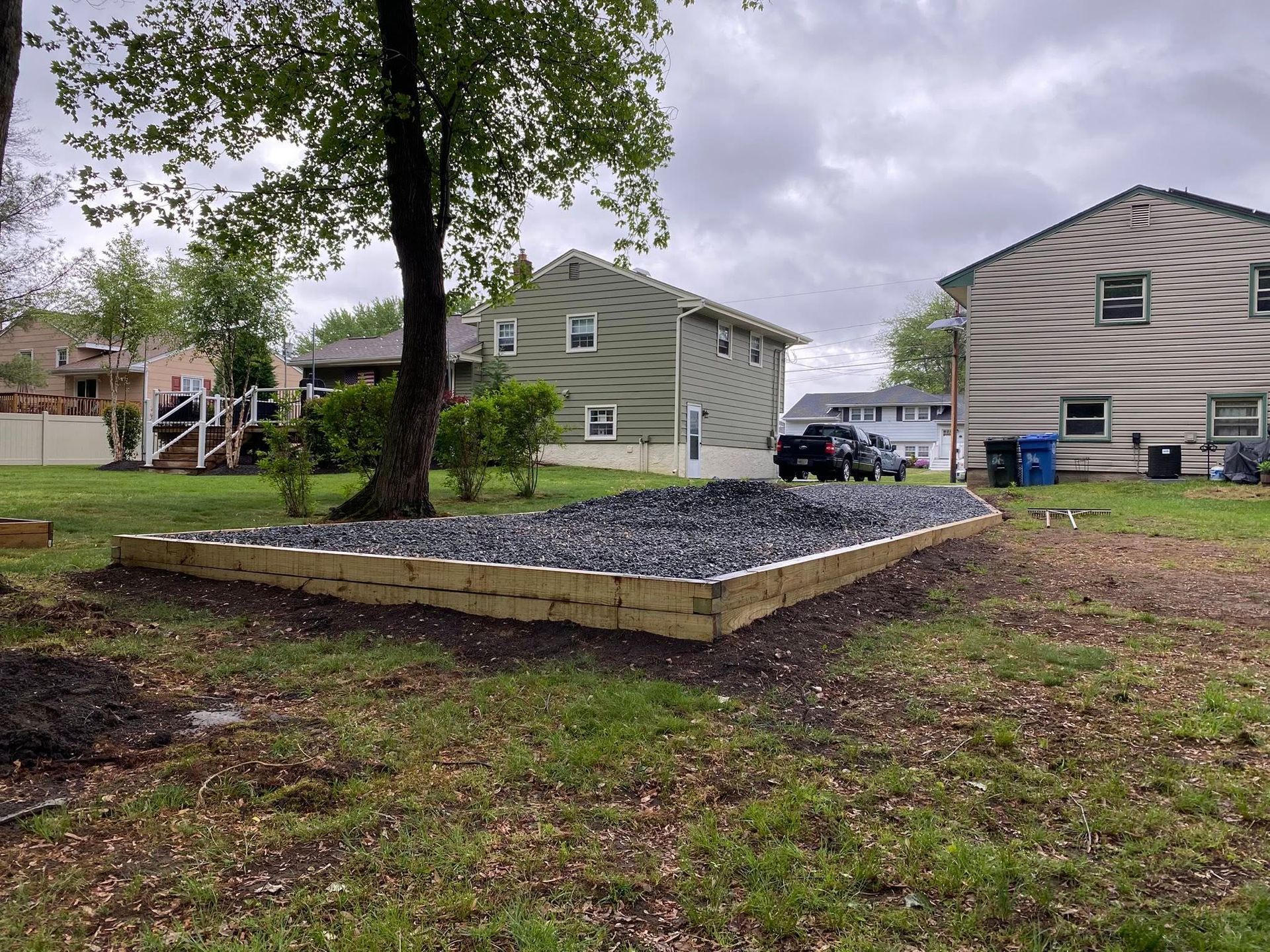 Raised garden bed filled with dark gravel, bordered by wooden planks, in a grassy yard.
