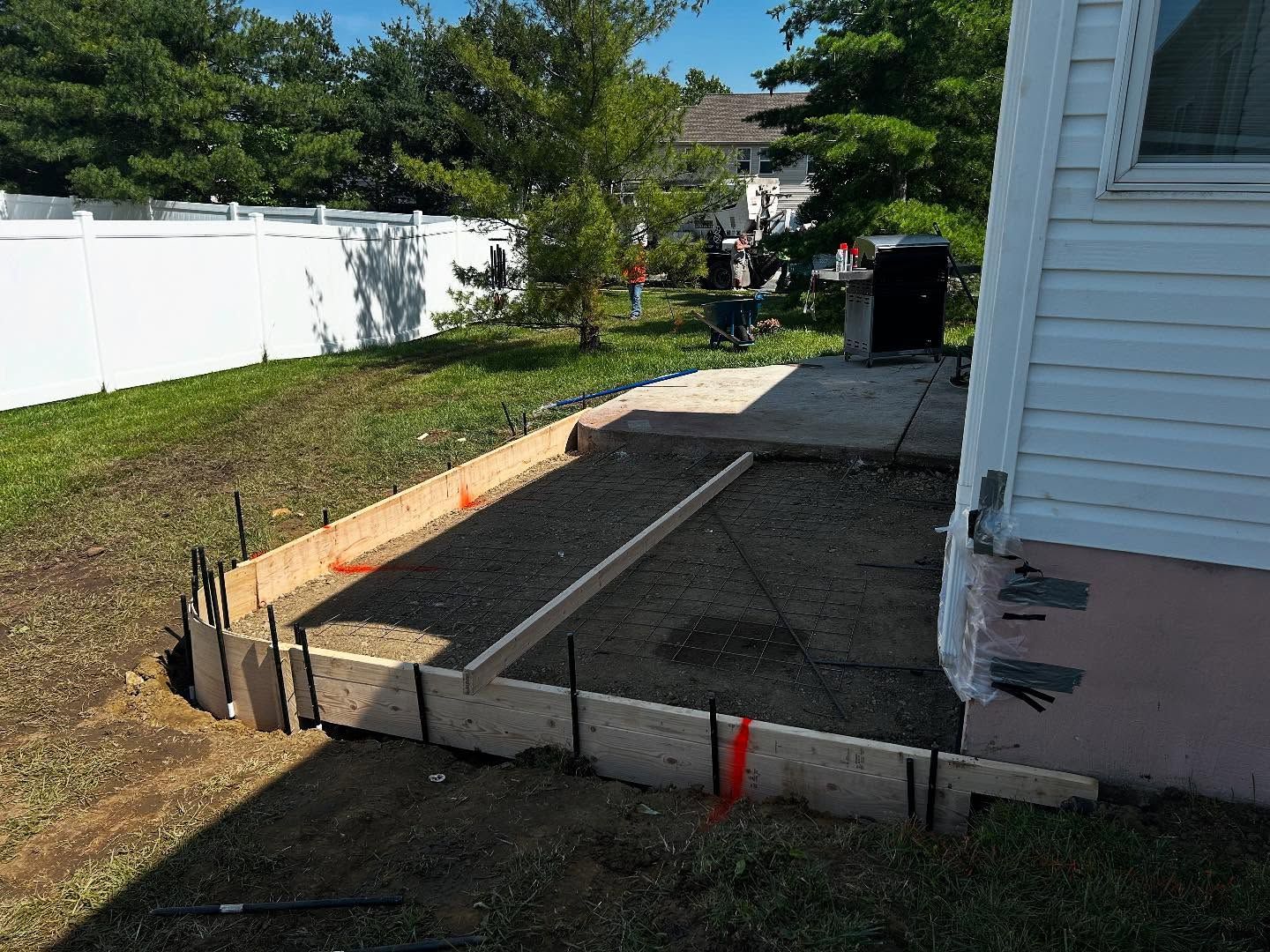 Wooden forms frame an outdoor area being prepared for concrete, near a house with white siding.
