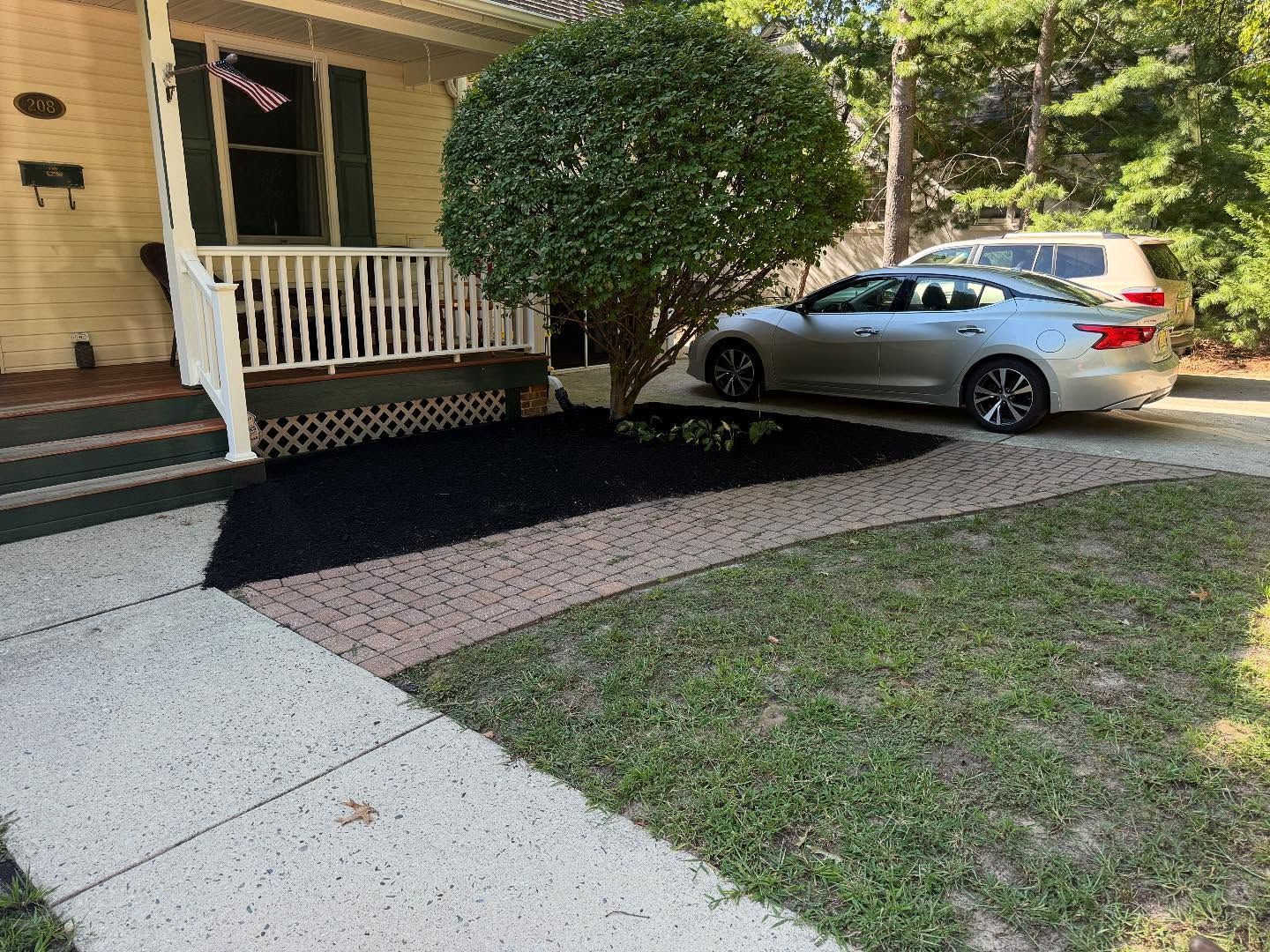 A house with a small porch, a tree in a landscaped bed, and a car parked in the driveway.