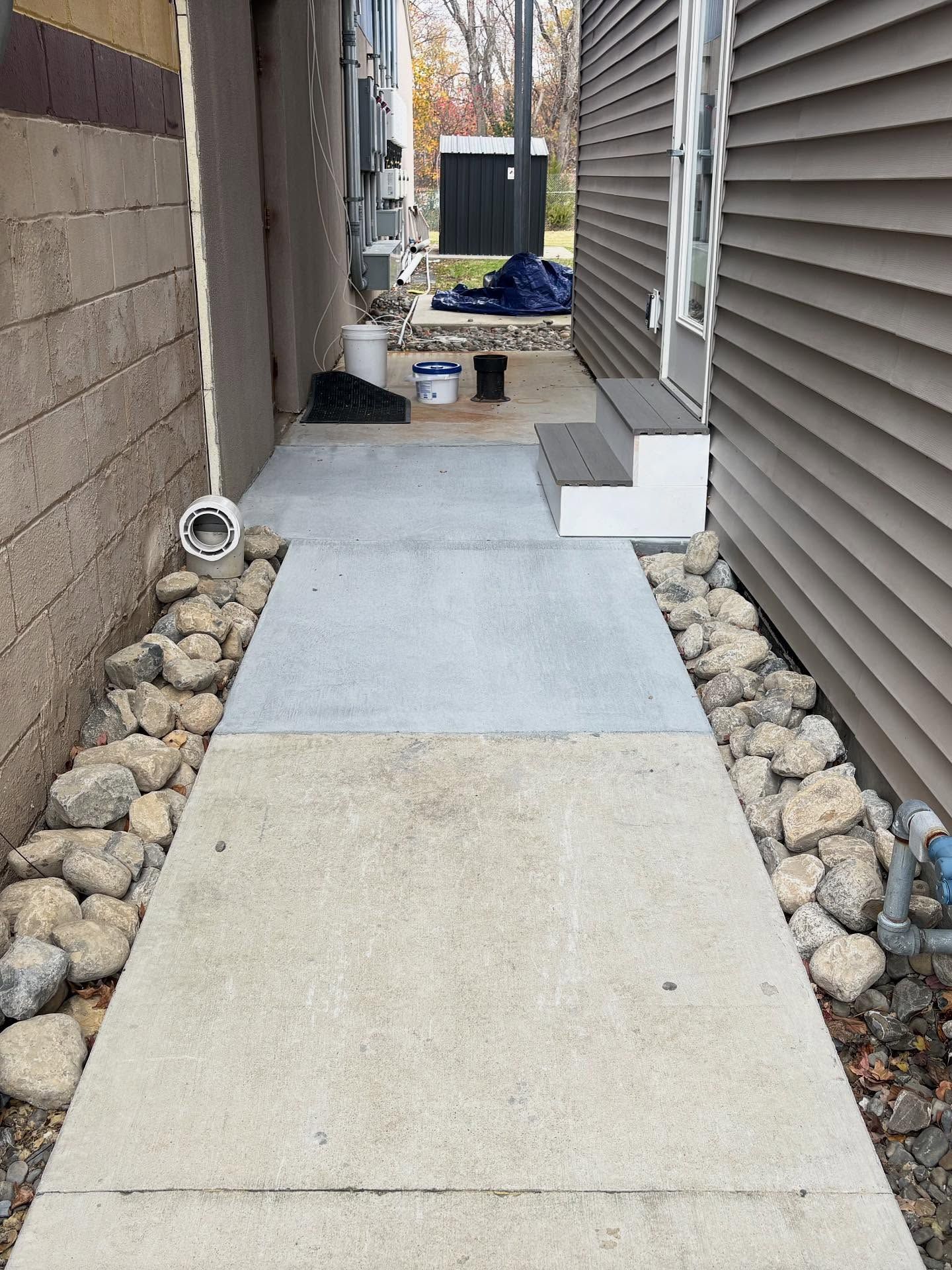 Concrete walkway with rock borders and two steps leading to a door.