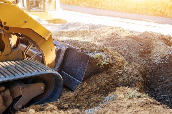 Bulldozer pushing gravel on a construction site; sunny outdoors.