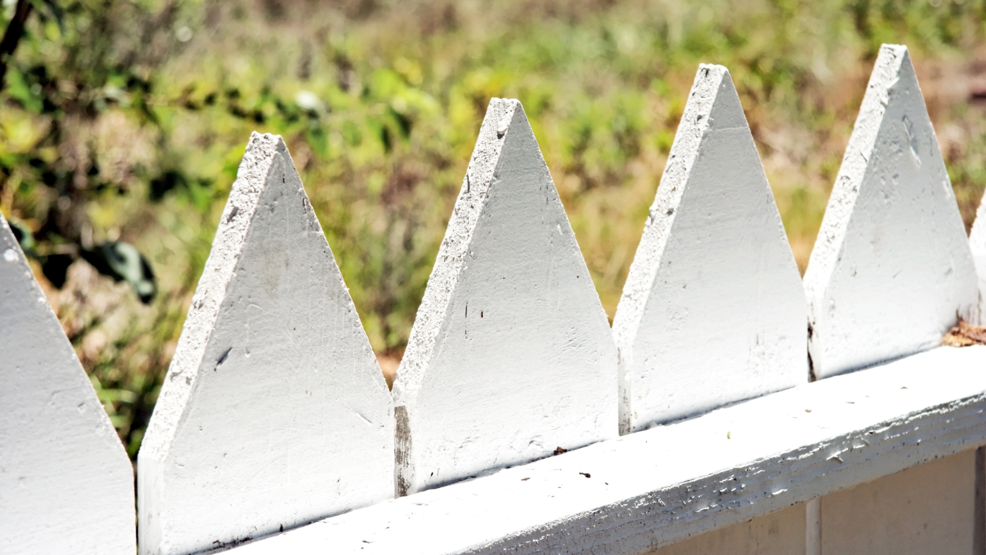 White triangular-topped concrete fence in front of blurred greenery.