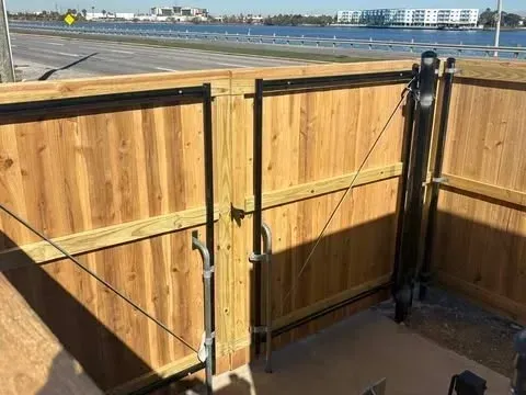 Wooden gate with metal hardware, opening to a view of water and buildings.