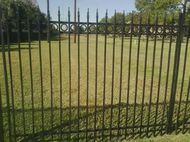 Black metal fence in a grassy field on a sunny day.