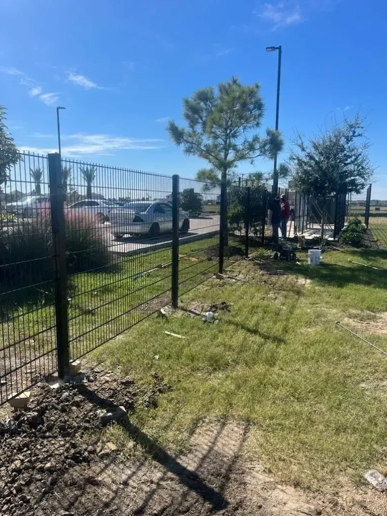 Black metal fence in a grassy area with workers nearby on a sunny day.