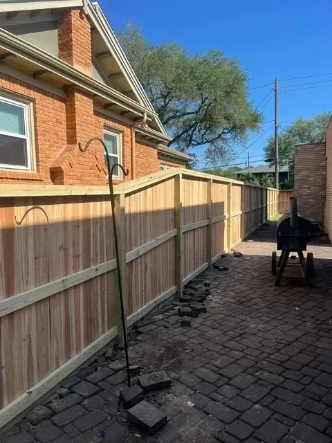 A newly constructed wooden fence lines a brick paved alley next to a brick building.