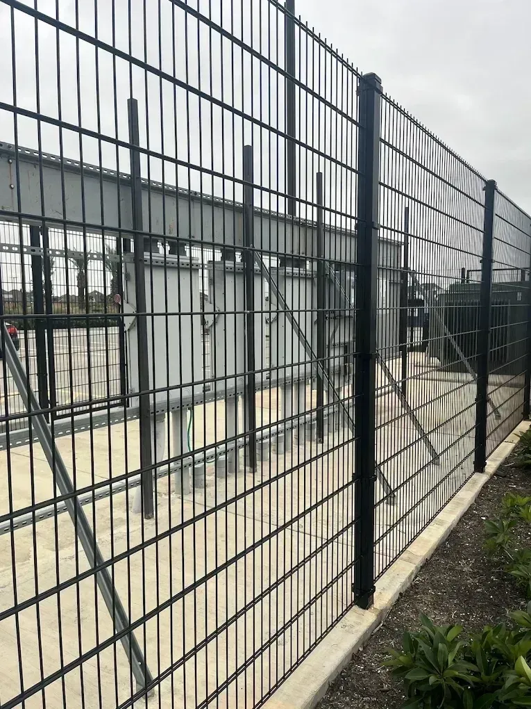 Black metal security fence surrounding an industrial structure. Concrete base and overcast sky.