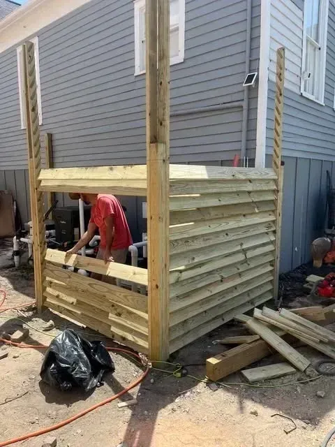 A wooden structure under construction next to a house; a person in a red shirt works inside.