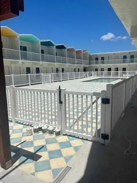 White fenced pool area with colorful motel rooms in the background on a sunny day.
