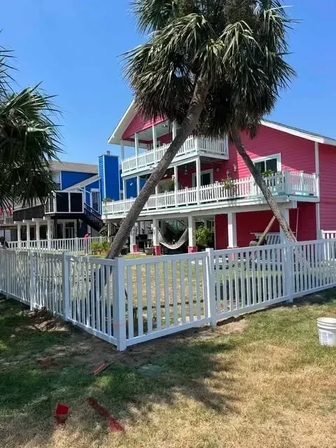 Pink house with white fence, palm trees, and blue sky.
