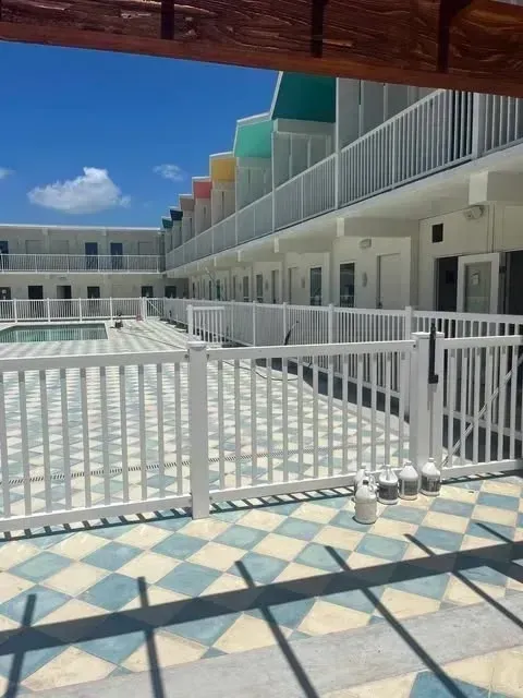 Courtyard motel with a white fence, pool, and rooms with colorful awnings. Blue and white tile.