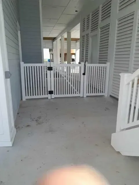 White picket gate on a concrete porch, leading to an open area with columns.