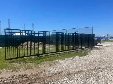 Black metal sliding gate in a gravel area under a blue sky.