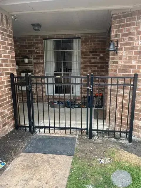 Black metal gate in front of a brick building. The gate is locked. A small welcome mat sits at the entrance.