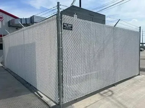White privacy fence with chain link and razor wire, surrounding an industrial building.