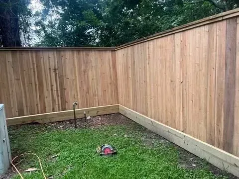 Wooden fence corner in a grassy yard, with a saw on the ground.