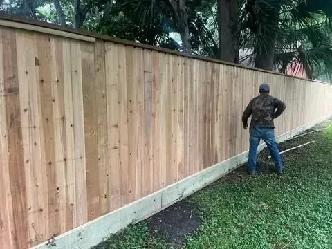 Man standing by new wooden fence in a yard with grass.