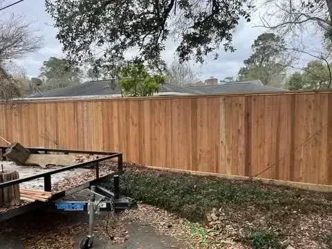 Tall wooden fence in backyard. A small trailer sits in front of it. Overcast sky.