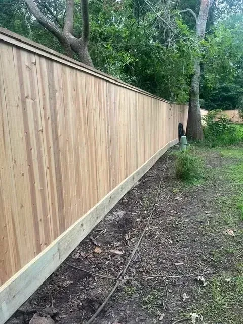 Wooden privacy fence curving along a grassy yard, trees in the background.