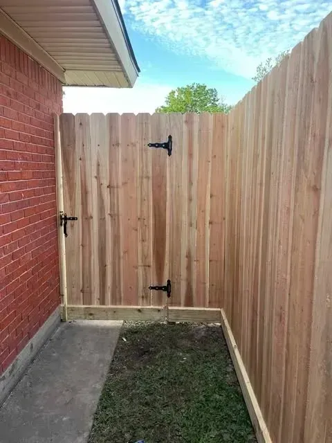 Wooden gate and fence next to a red brick wall, on a patch of grass.