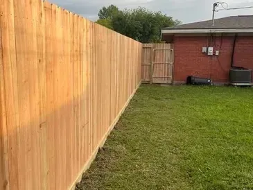 Wooden fence along a grassy backyard, with a gate leading to a brick house.