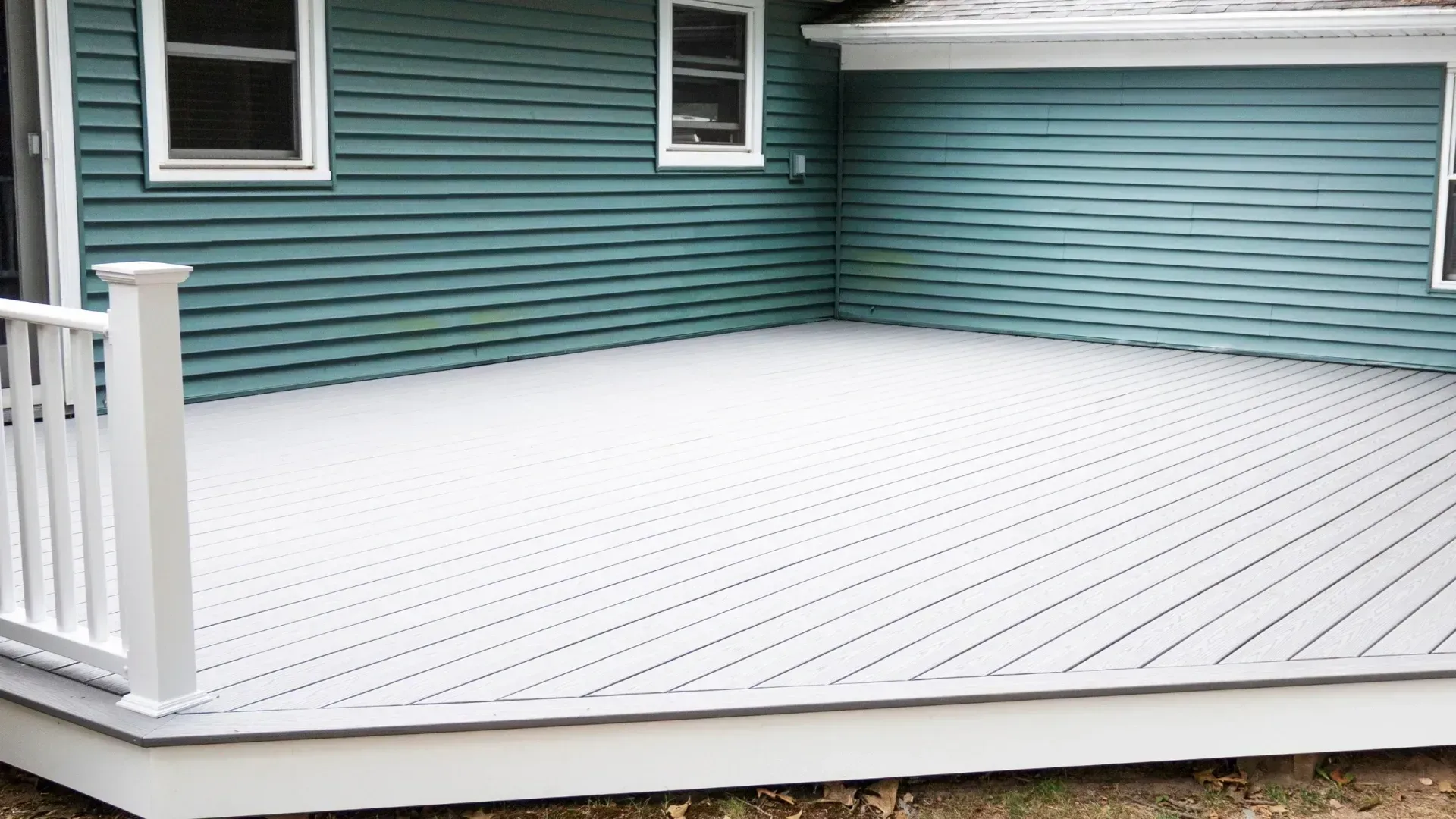 White composite deck with railing, adjacent to a teal-sided house with white trim.