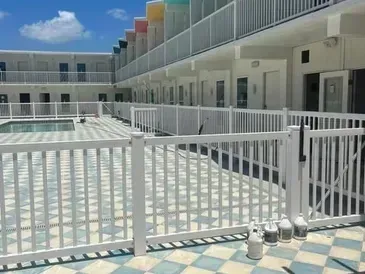 Courtyard with pool, white fences, and a multi-colored hotel facade under a blue sky.