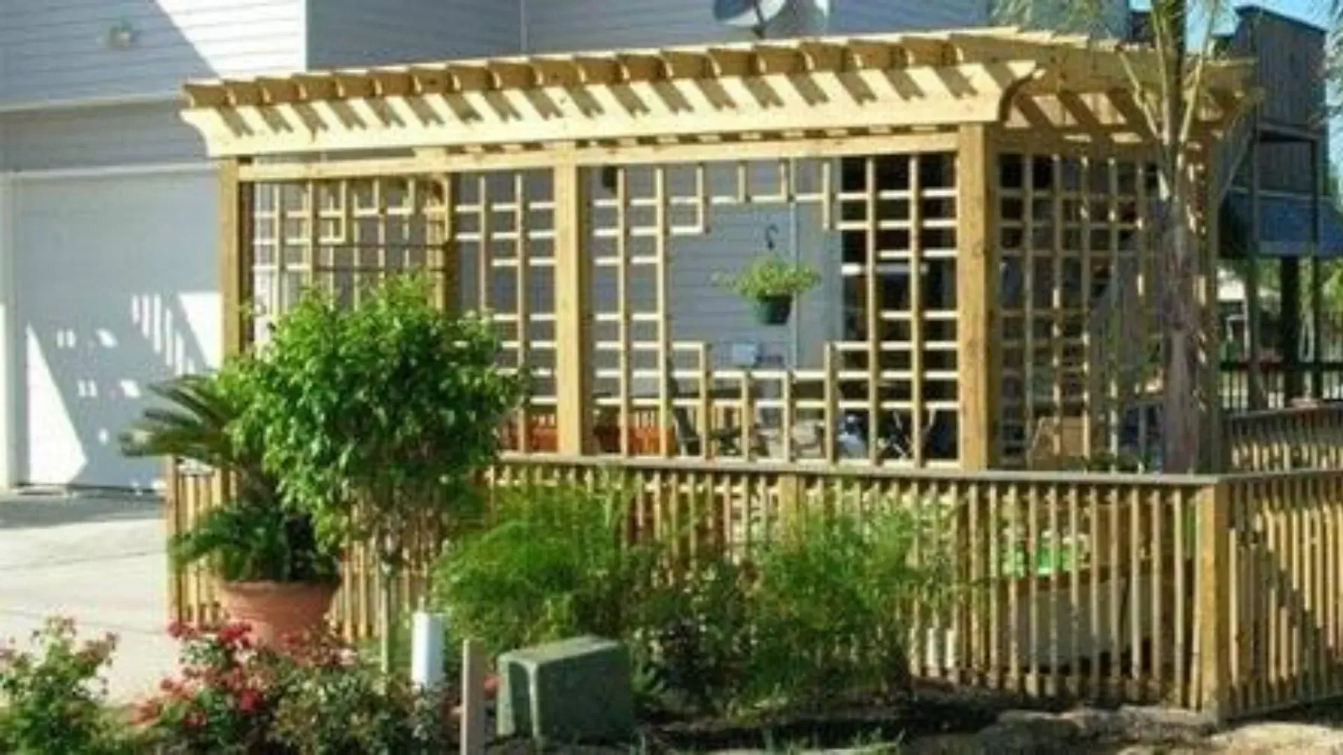 Wooden trellis structure with lattice walls and fence, surrounded by greenery.