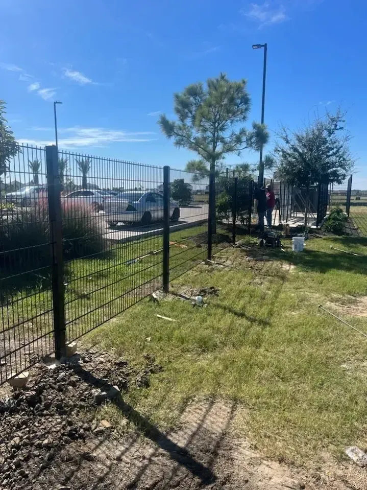 Black metal fence being installed near a grassy area, a tree, and a parking lot.
