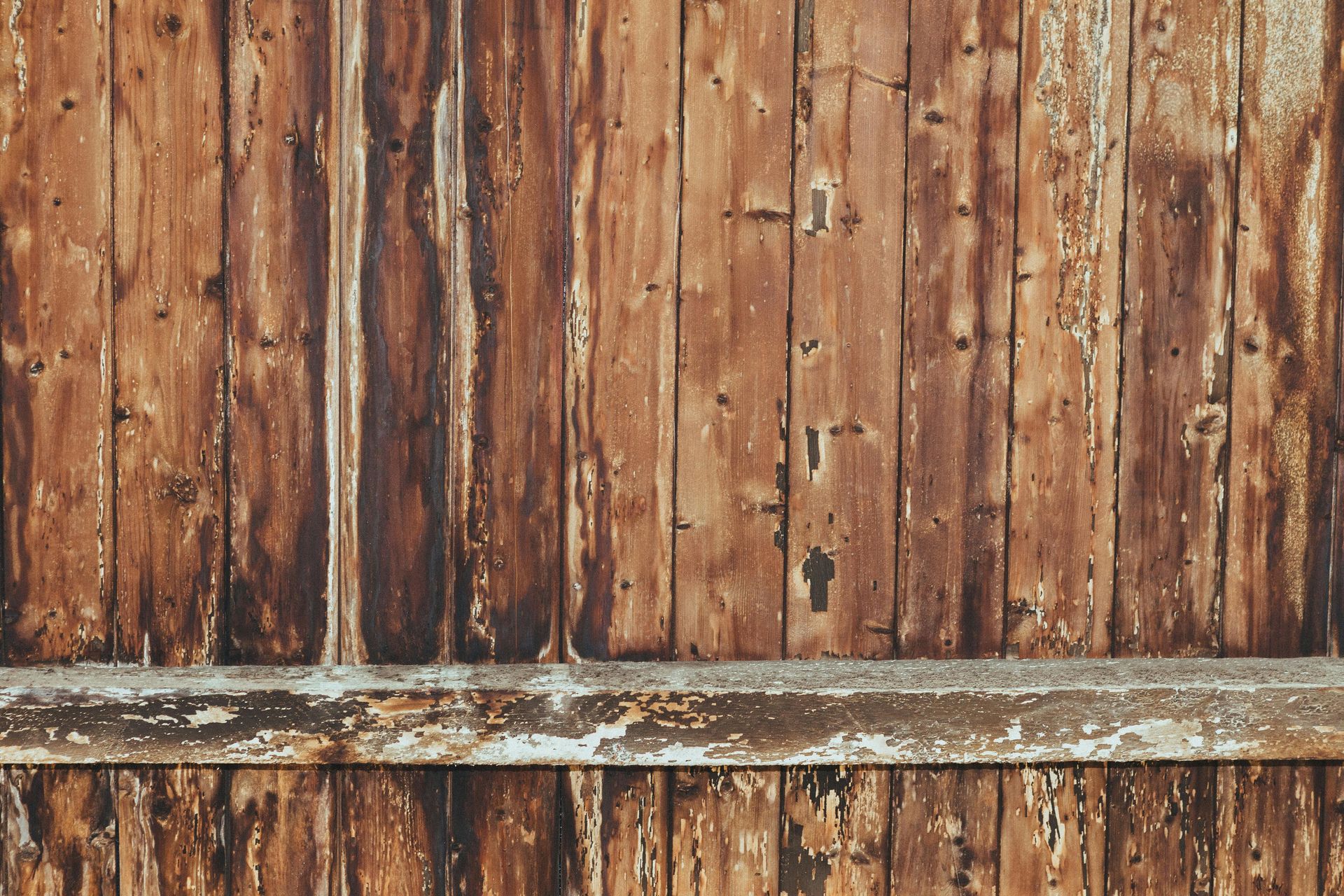Weathered wooden fence with vertical slats and a horizontal support beam, showing peeling paint and wood grain textures.