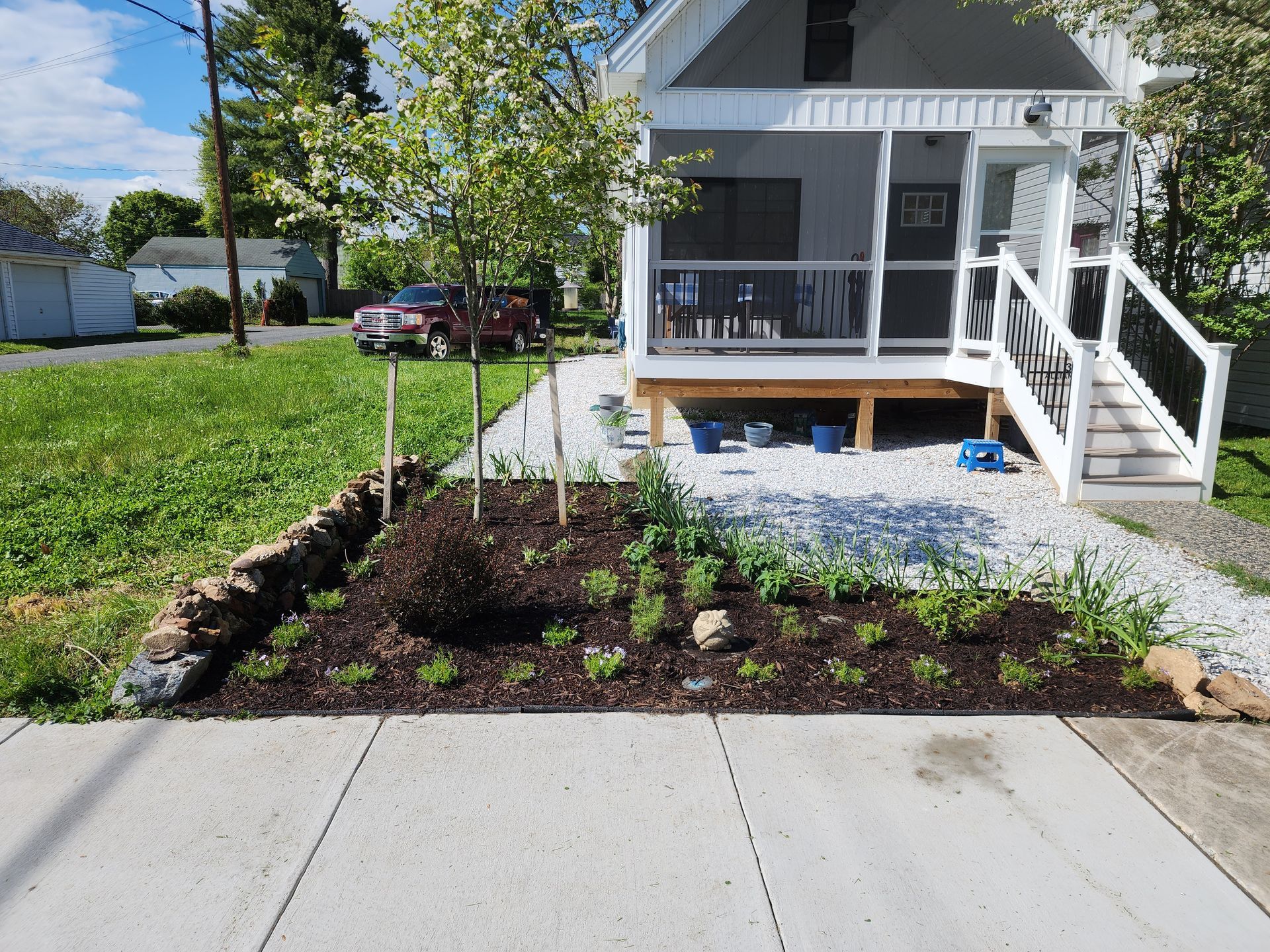 Small house with a porch, garden bed with plants and mulch, white gravel path along the front.